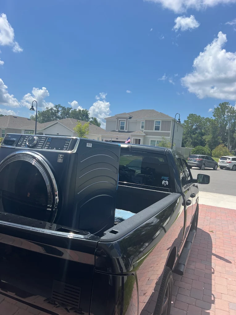 Dark front-loading laundry appliance in the bed of a pickup truck